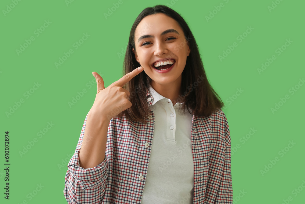 Young woman pointing at her teeth on green background