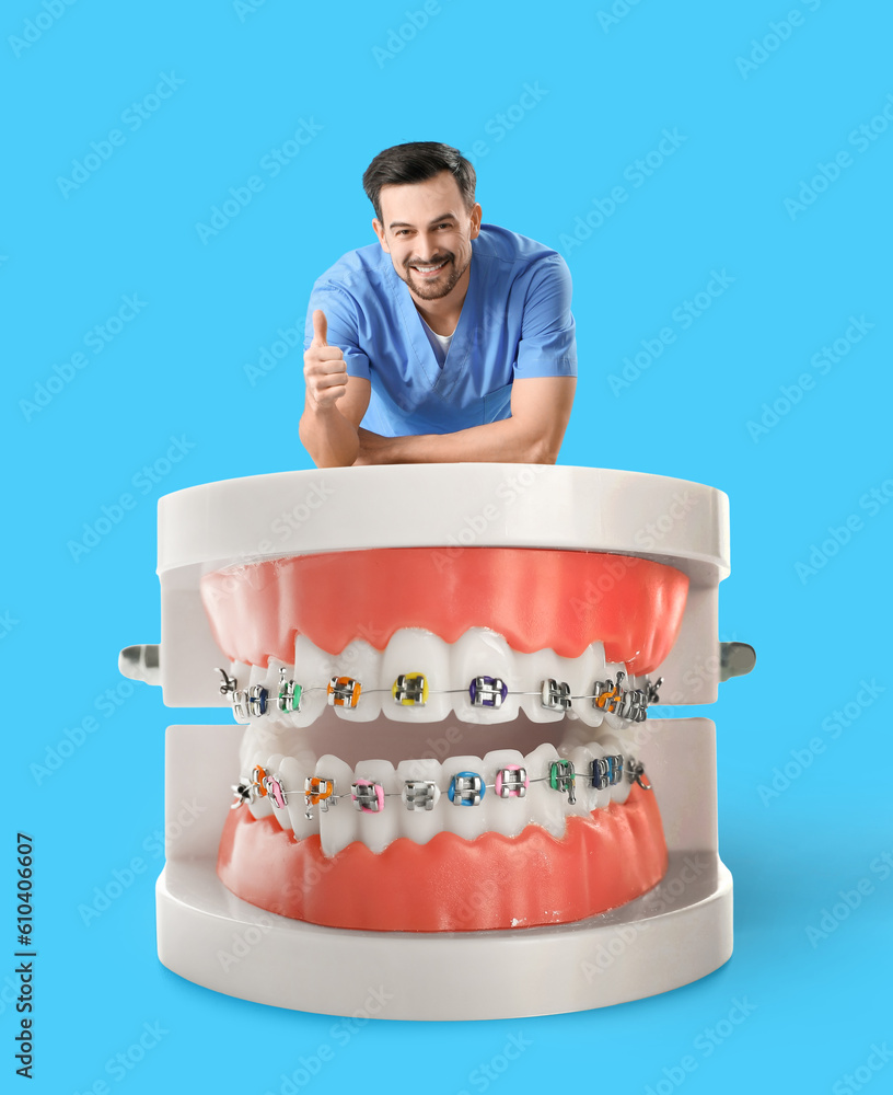 Male dentist and big plastic jaws with braces on light blue background