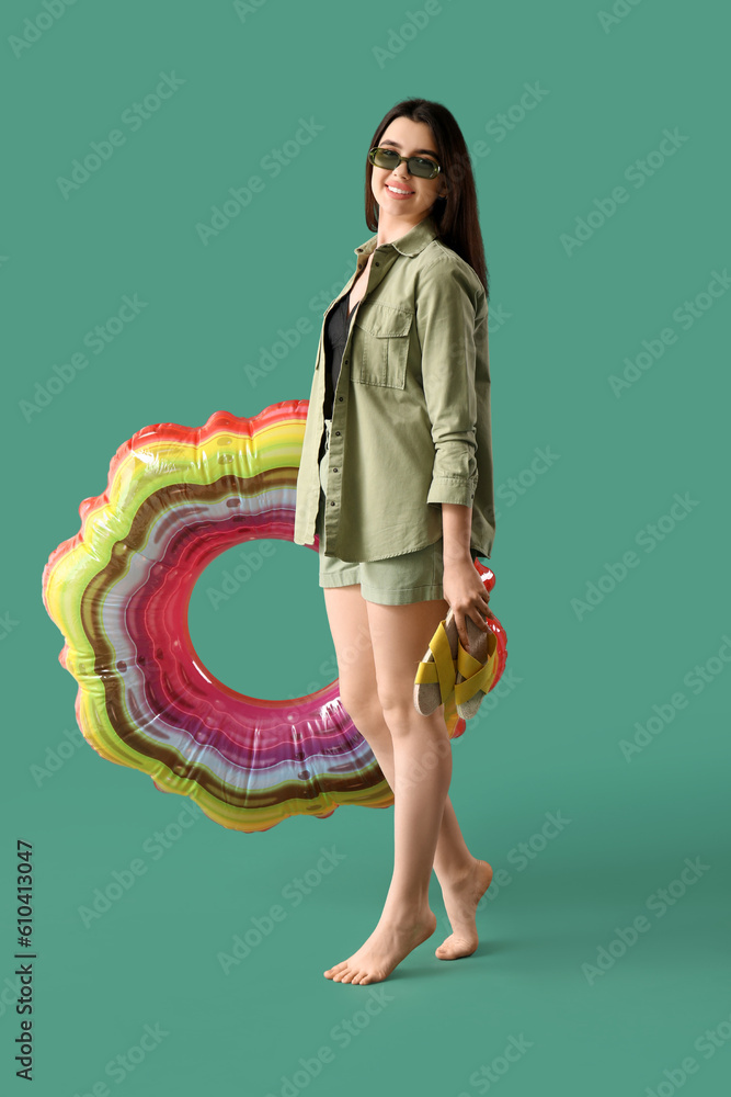 Young woman with flip-flops and inflatable ring on green background