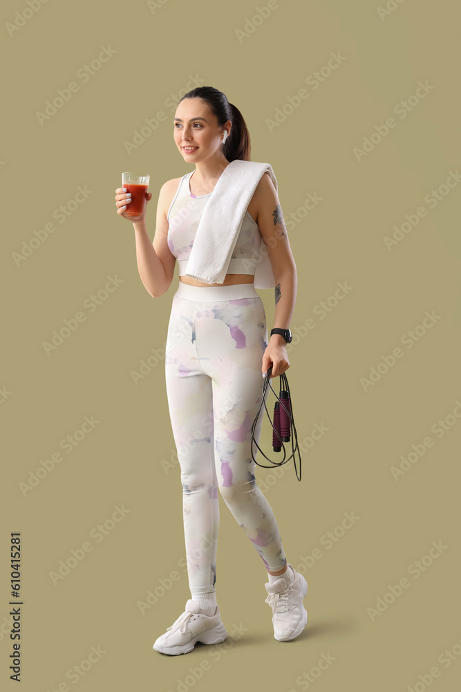 Sporty young woman with skipping rope and glass of vegetable juice on green background