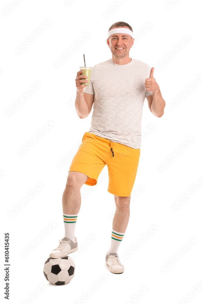 Sporty mature man with glass of vegetable smoothie and soccer ball showing thumb-up on white backgro
