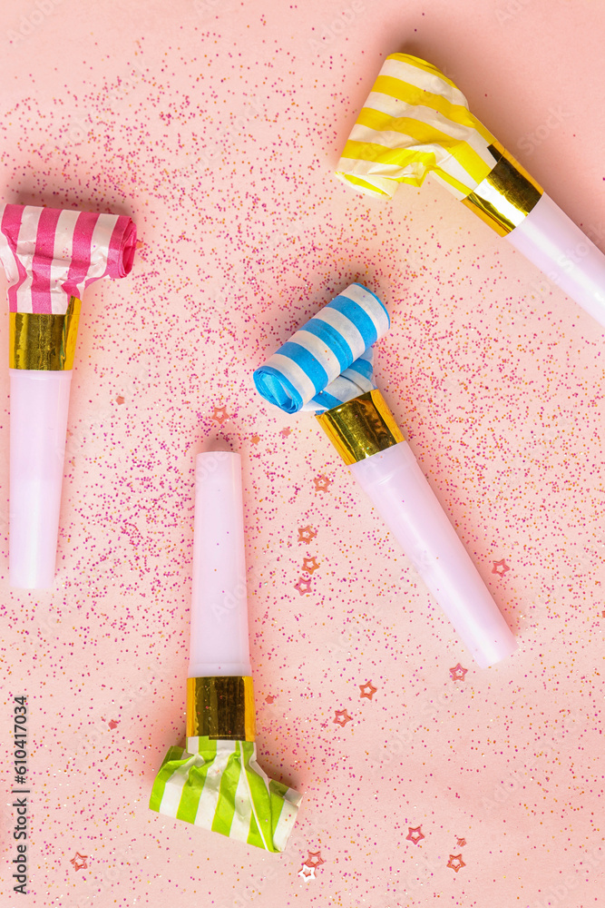 Composition with whistles and sequins for birthday party on pale pink background