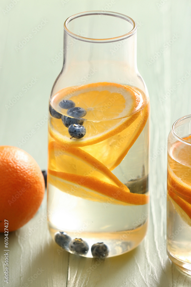Glass and bottle of infused water with orange slices on light wooden background