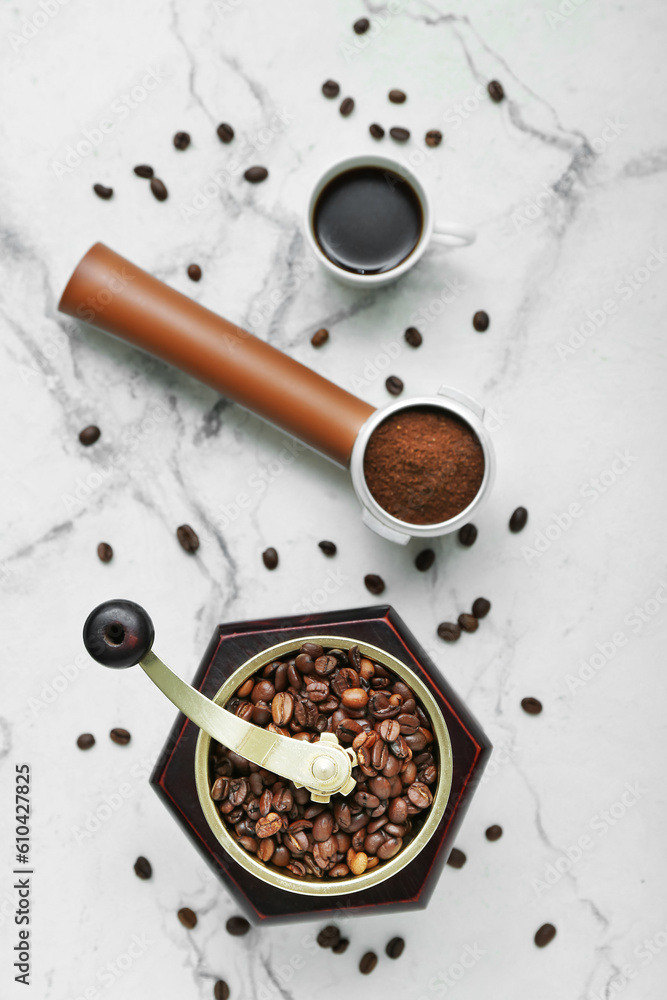 Cup of hot espresso, coffee grinder, beans and portafilter on white marble background