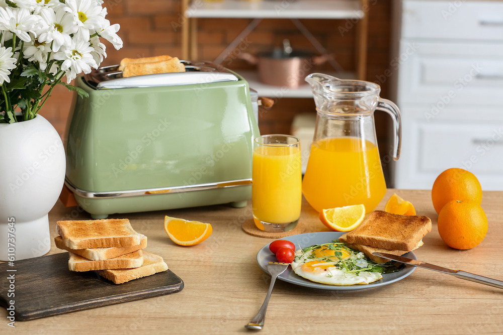 Modern toaster, fried eggs and healthy orange juice on table in kitchen