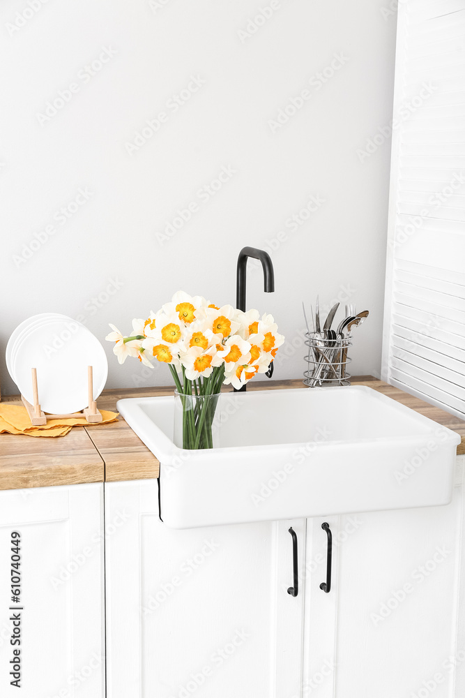 Vase with blooming narcissus flowers in sink