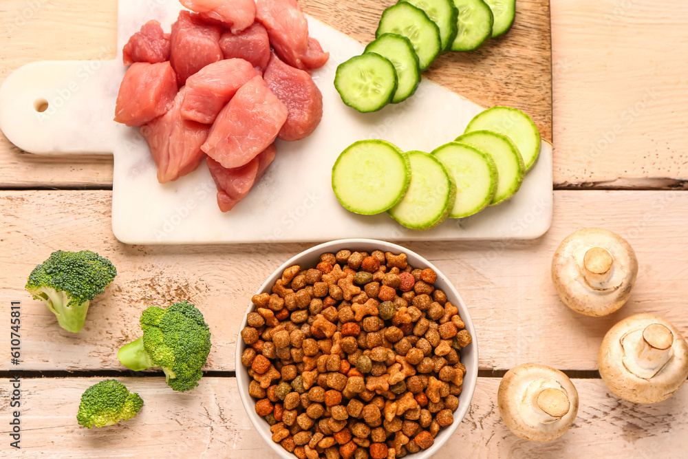 Composition with dry pet food, raw meat and natural products on light wooden background