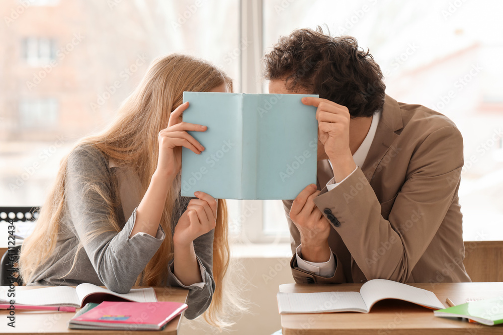 Teenage couple covering themselves with book in classroom