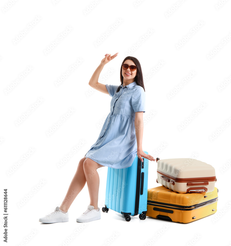 Young woman with suitcases showing victory gesture on white background