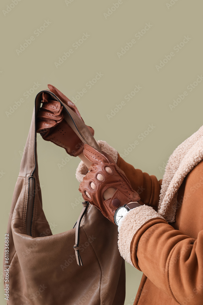 Stylish young woman in leather gloves with bag on green background, closeup
