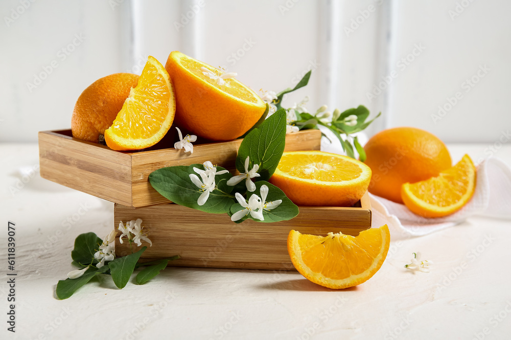 Wooden box of oranges with blooming branch on white table