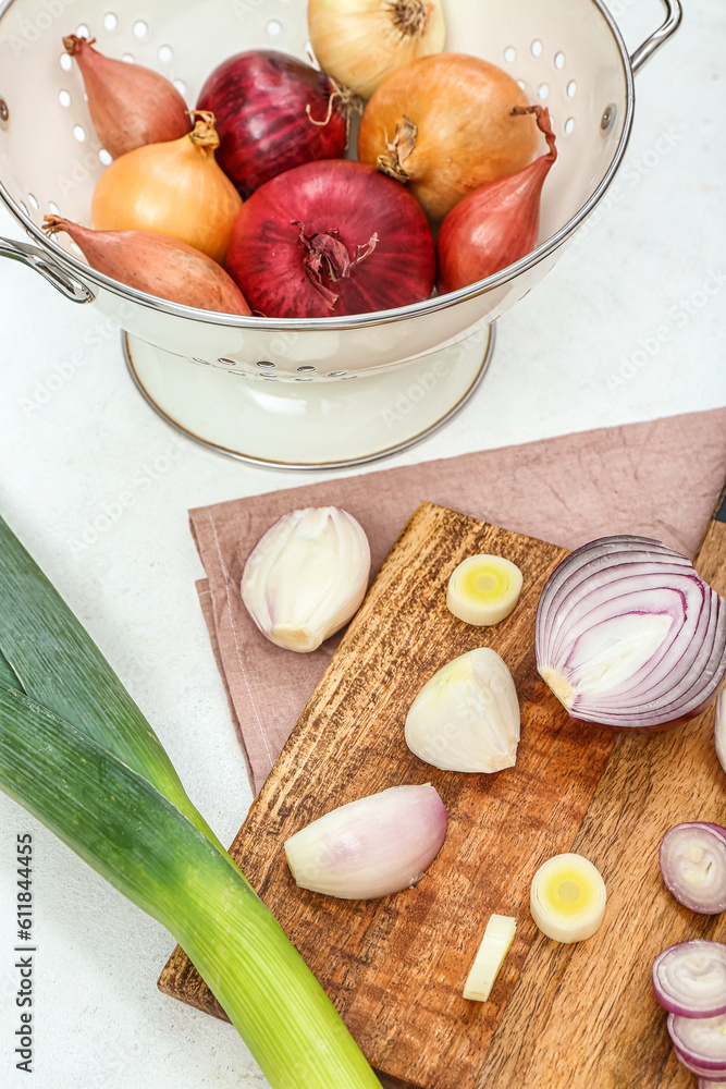 Wooden board and colander with different kinds of onion on white background