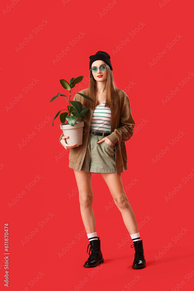 Stylish young woman with houseplant on red background