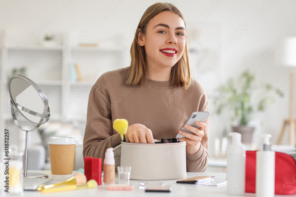 Young woman with cosmetic bag and mobile phone at home
