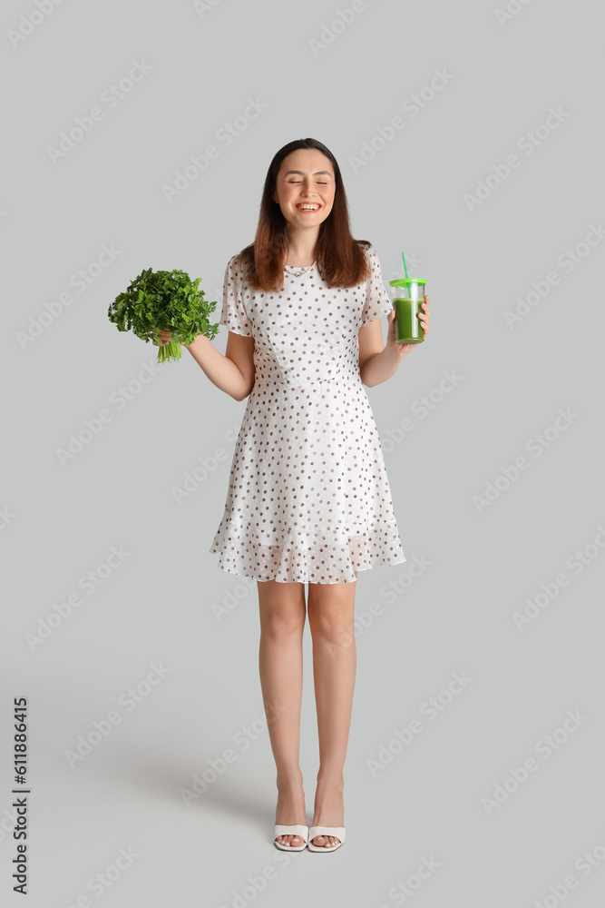 Young woman with glass of vegetable juice and parsley on grey background