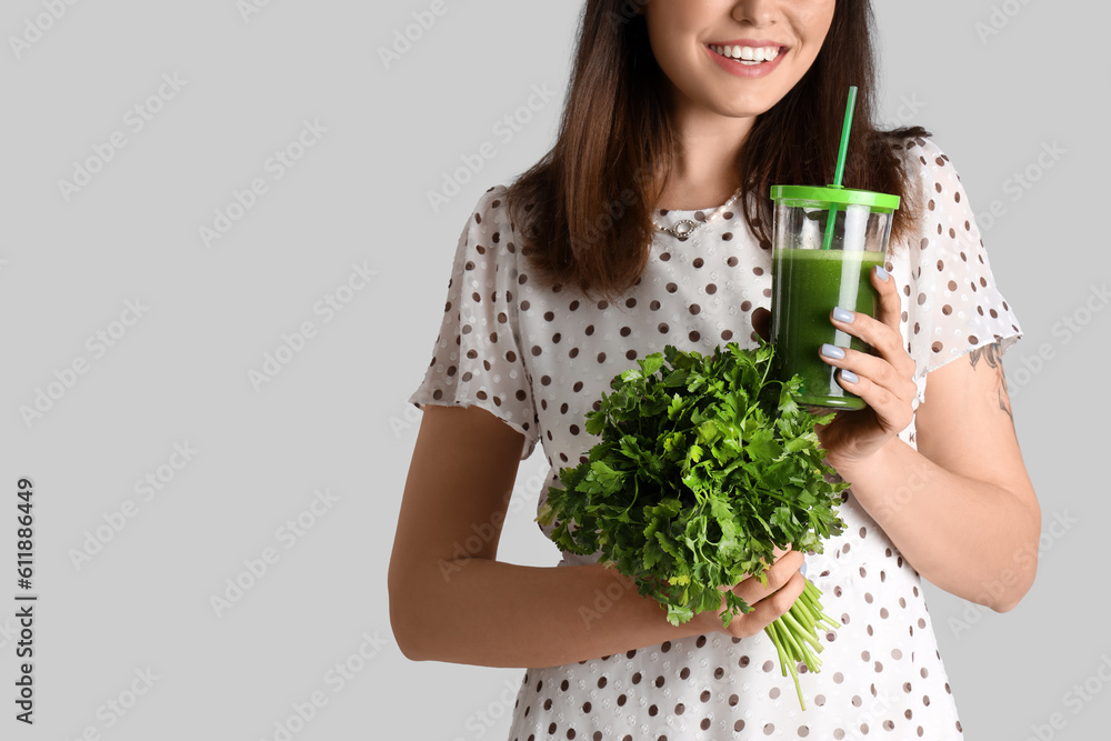 Young woman with glass of vegetable juice and parsley on grey background, closeup