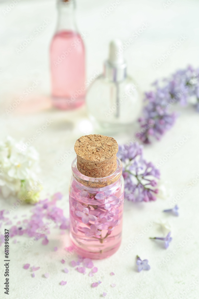 Bottles of cosmetic oil with beautiful lilac flowers and sea salt on white table
