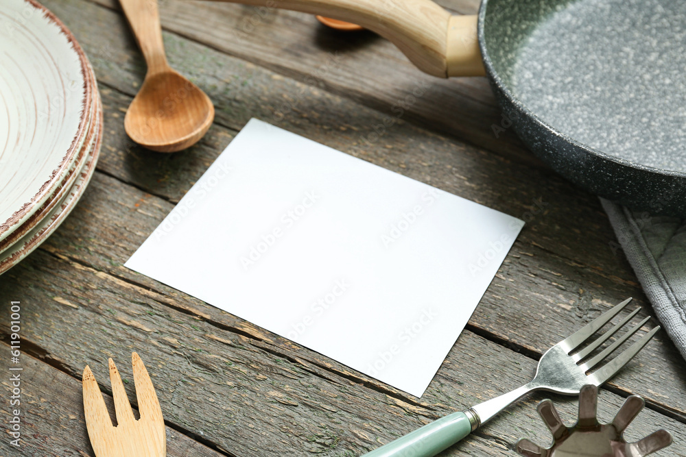 Blank card and different kitchen utensils on wooden background, closeup
