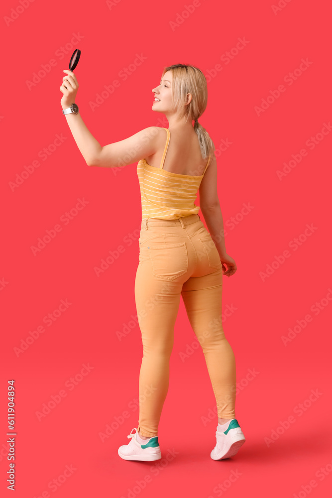 Young woman with magnifier on red background