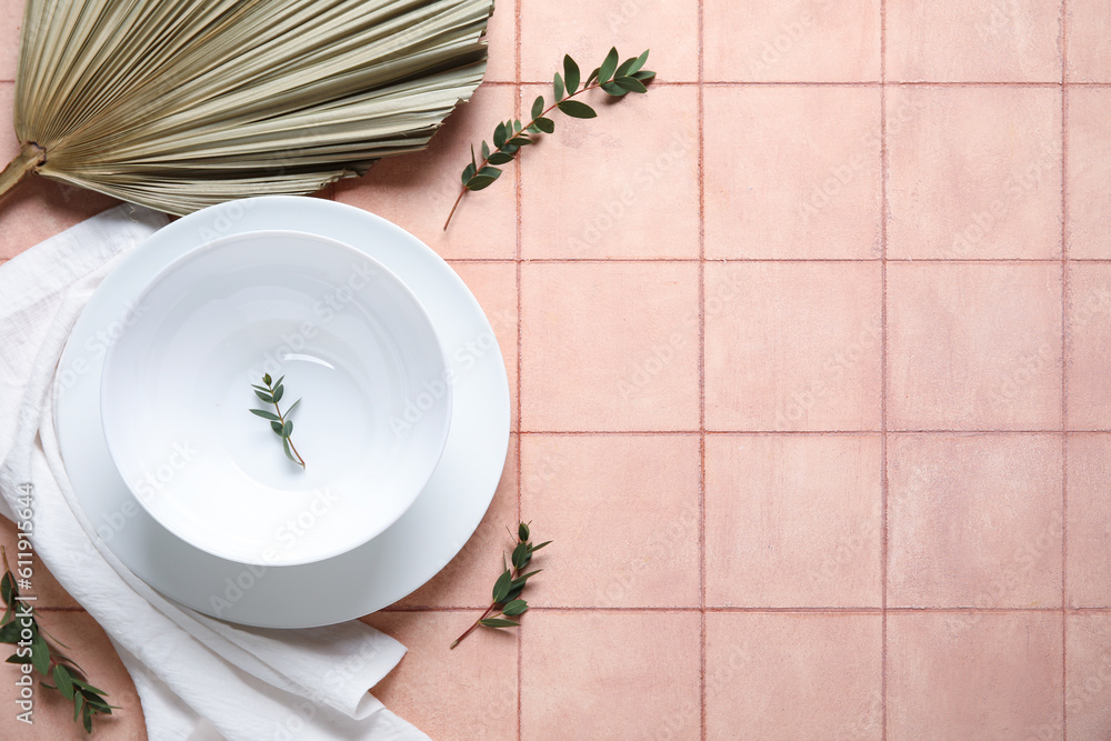 White plates with dry palm leaf on pink tile background