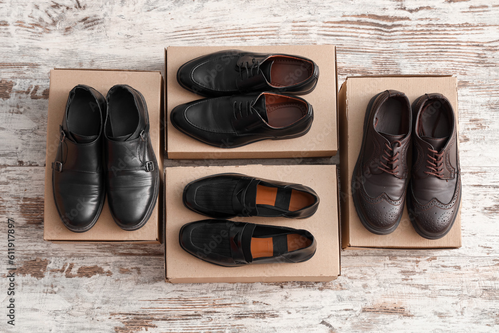 Cardboard boxes with different male shoes on light wooden background
