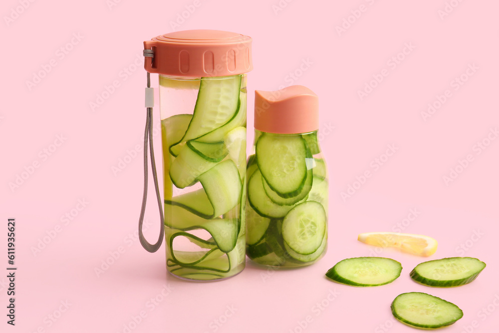 Sports bottles of infused water with cucumber slices on pink background