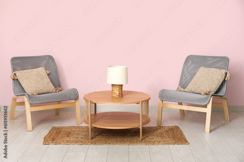 Armchairs with wooden coffee table, lamp and floor mat near pink wall