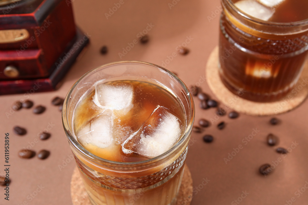 Glasses of ice coffee with beans and grinder on beige background
