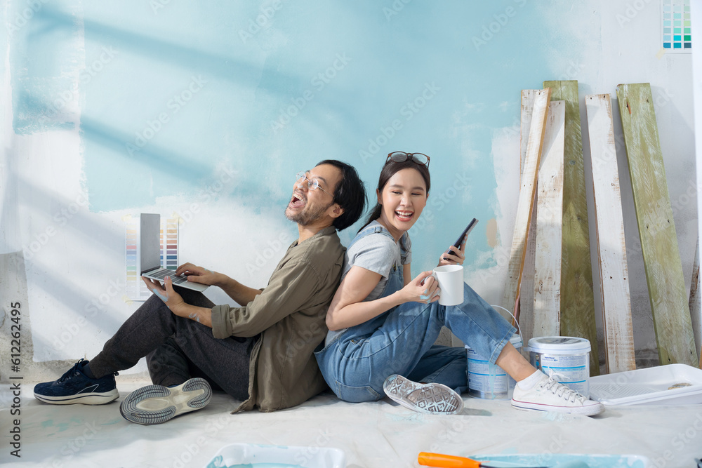 Young Asian couple repairing and painting the wall Sit and look at home decorating ideas through a l