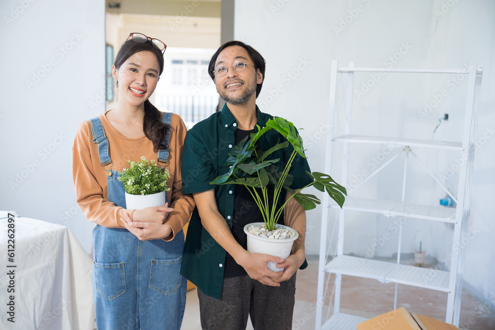 Portrait young couple moving to new house holding Flower Pots Plant Pots looking at camera at home