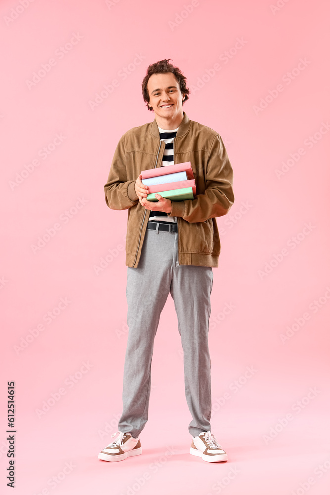 Young man with stack of books on pink background