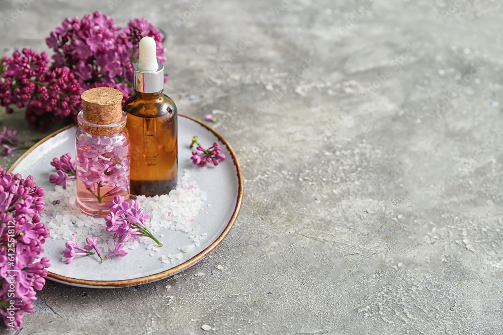 Bottles of cosmetic oil with beautiful lilac flowers and sea salt on grey table