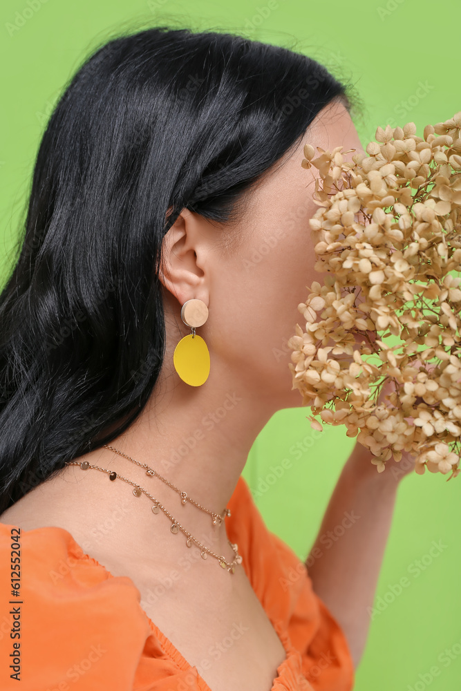 Profile of young woman wearing stylish jewelry with flowers near green wall