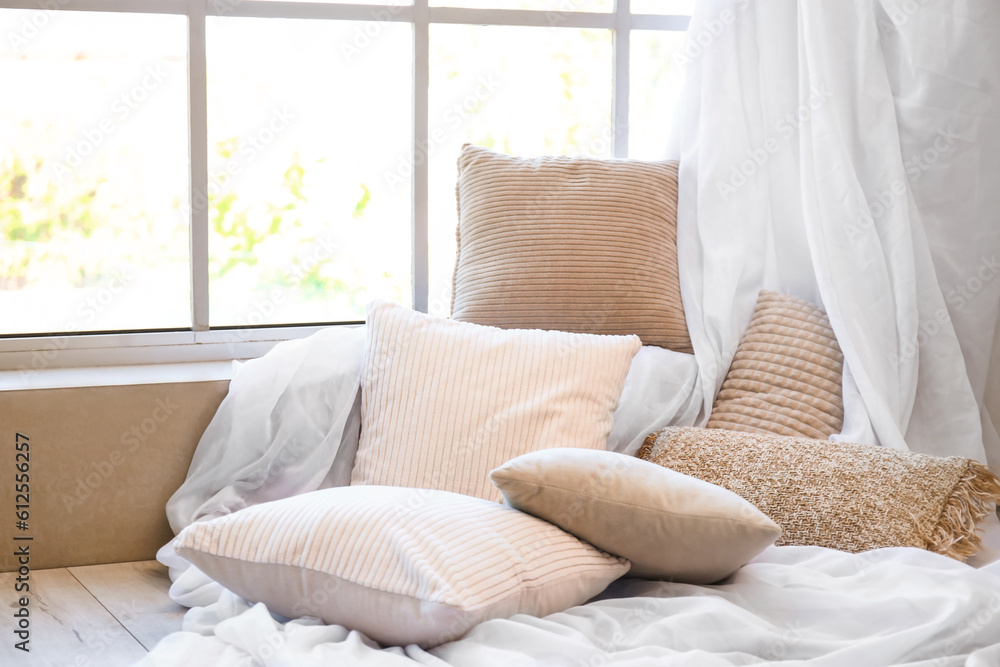 Stylish pillows with curtain near window in light room