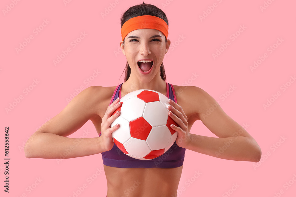 Sporty emotional woman with soccer ball on pink background