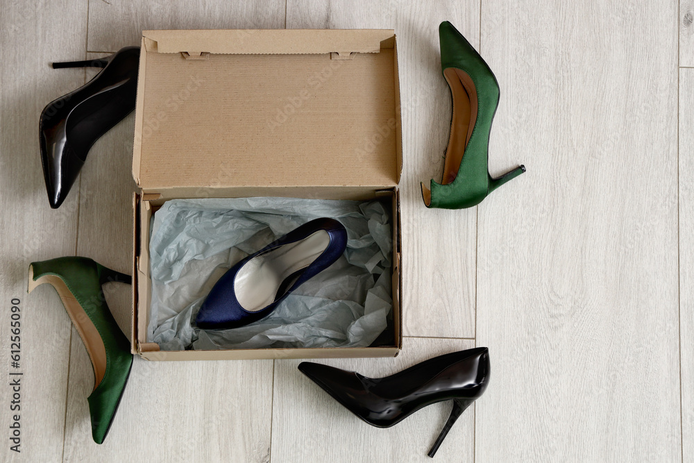 Cardboard box with high-heeled shoes on light wooden background