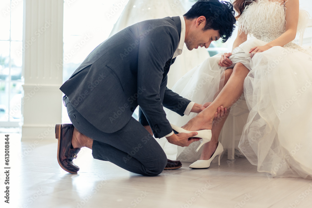 Asian beautiful bride trying on wedding shoes with her fiance in studio. 