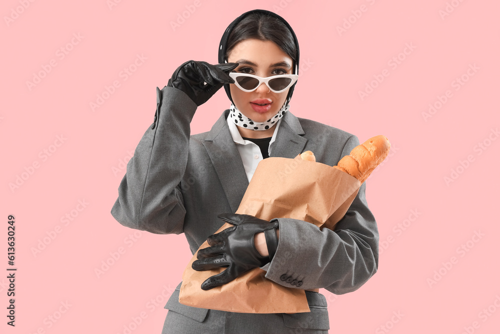 Stylish young woman in leather gloves with baguettes on pink background