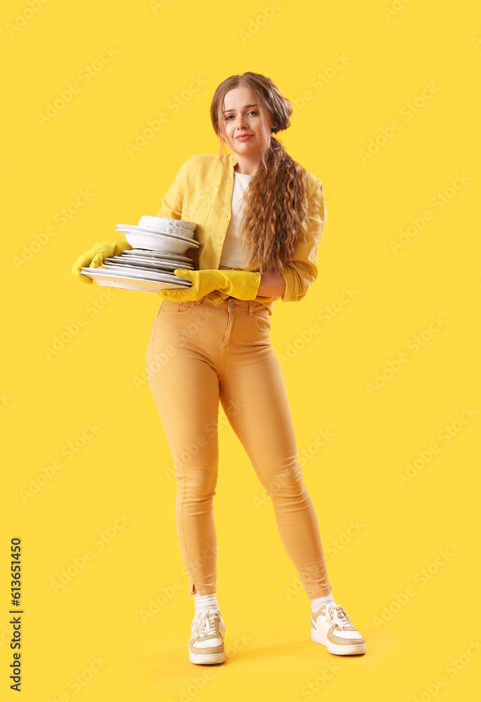 Sad young woman with many dirty dishes on yellow background