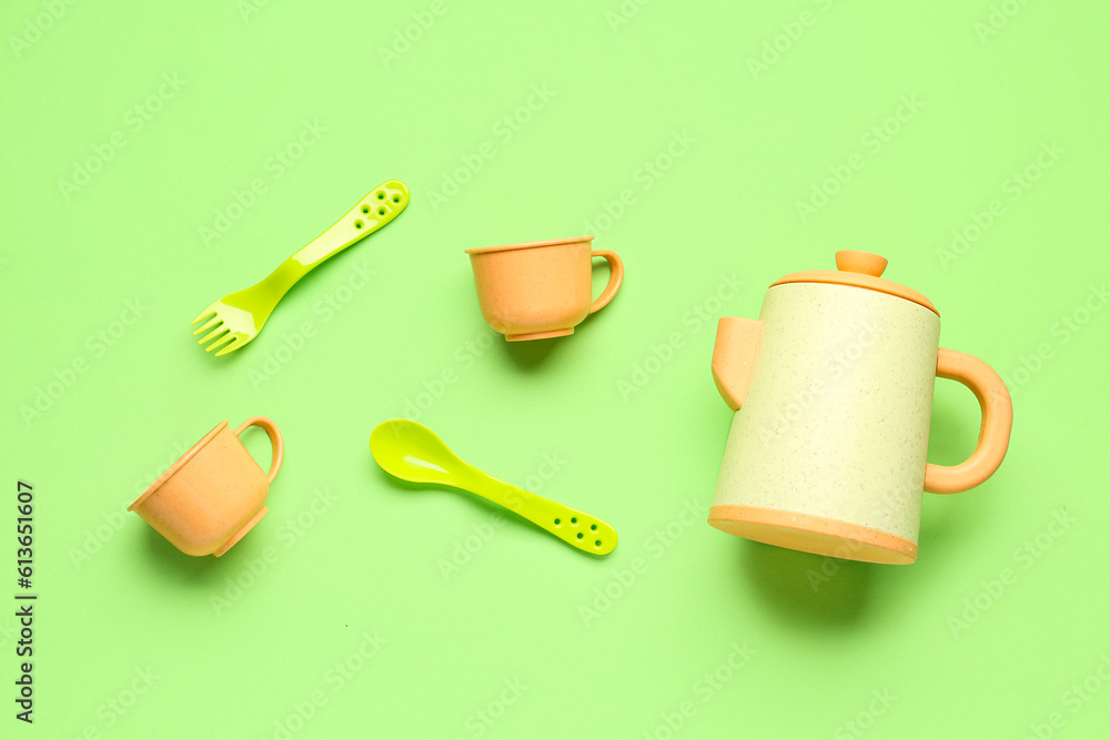 Teapot with cups and cutlery for baby on green background