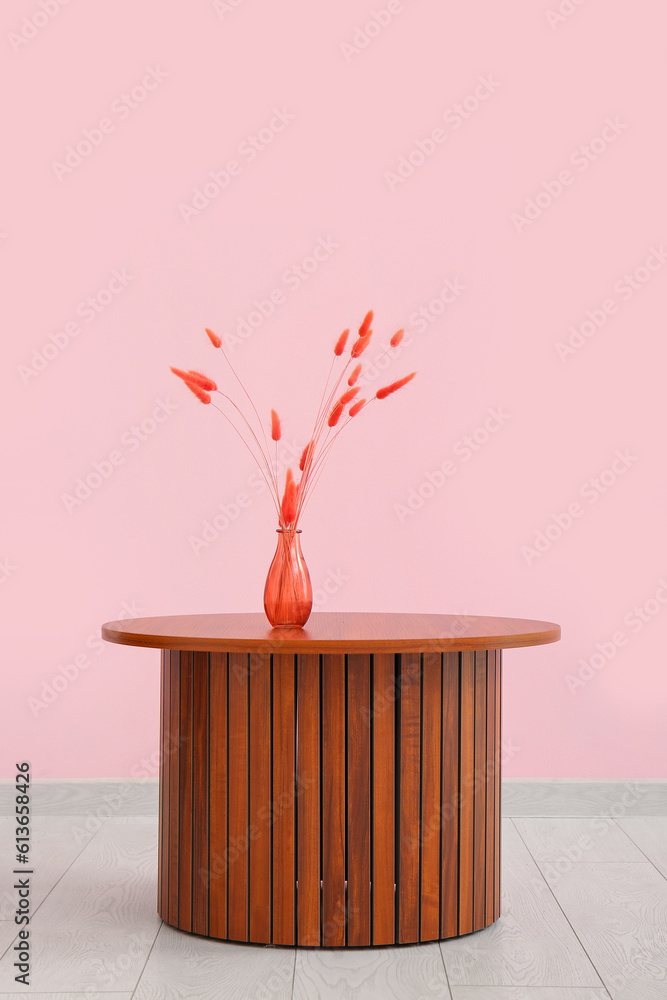 Wooden coffee table with red lagurus grass in vase near pink wall