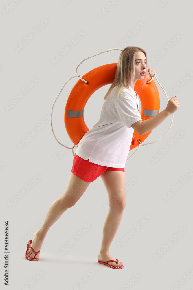 Female lifeguard with ring buoy running on light background