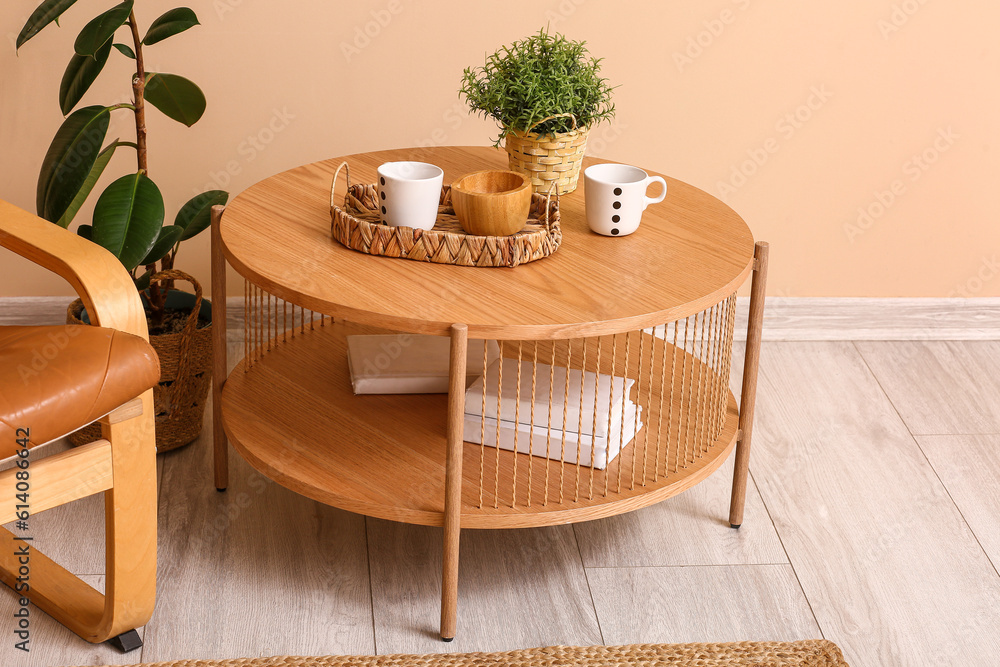 Wooden table with houseplant, cups and books near beige wall in room