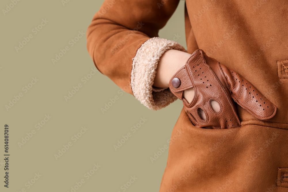 Stylish young woman in leather glove on green background, closeup
