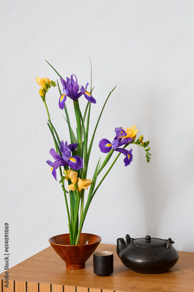 Beautiful ikebana with teapot and cup on table near light wall