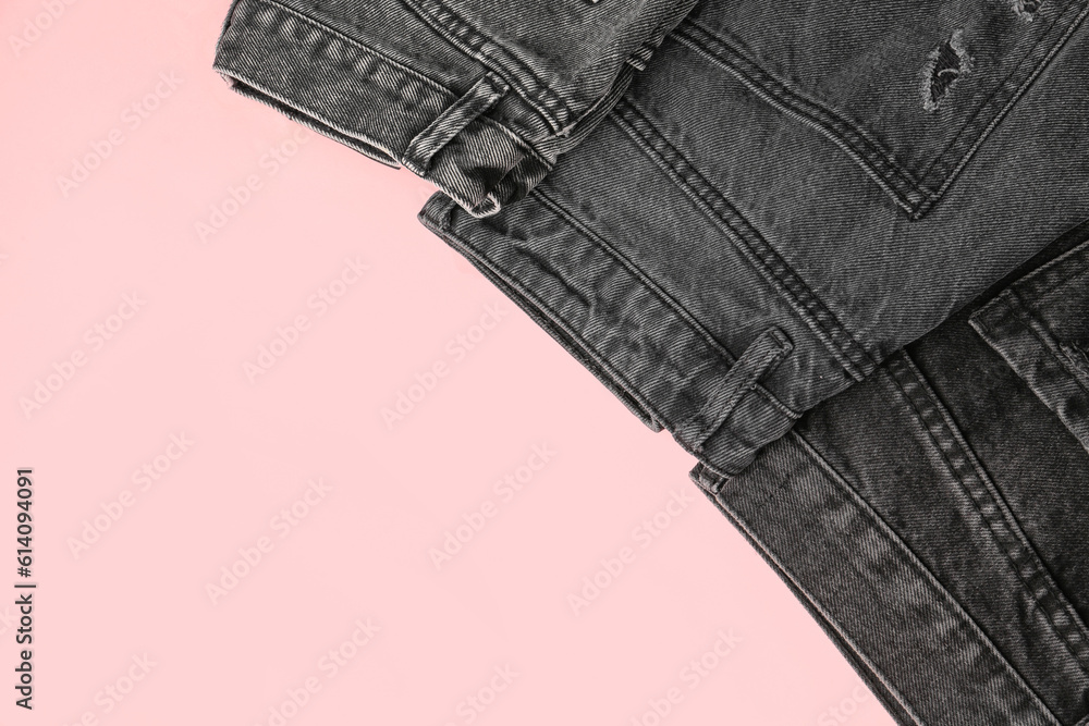 Different folded dark jeans on pink background
