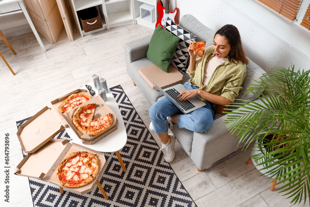 Beautiful woman with tasty pizza using laptop on sofa at home