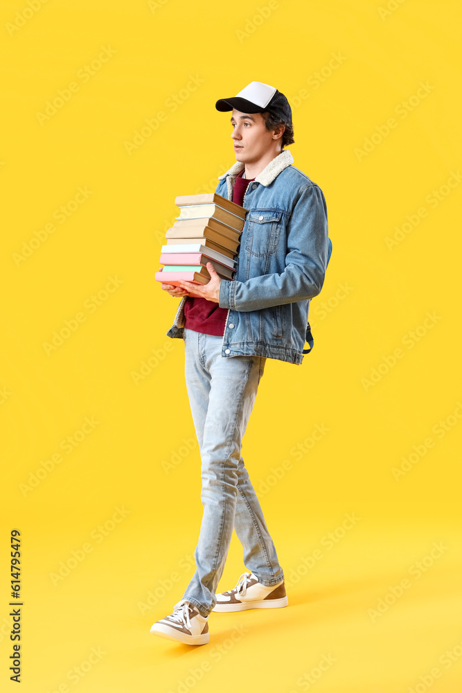Male student with stack of books on yellow background