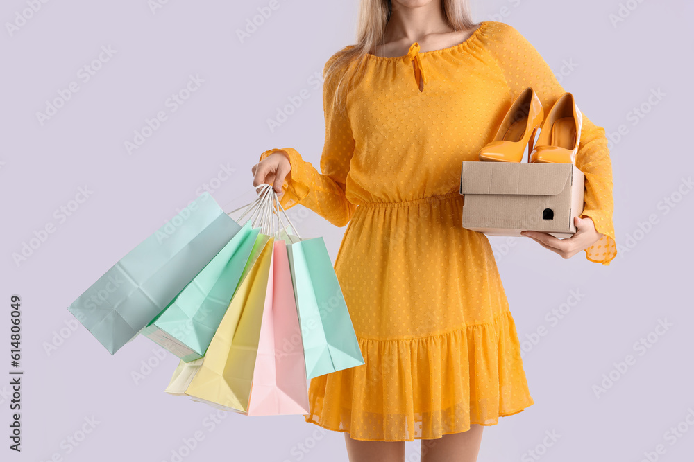 Young woman with shoes and shopping bags on light background
