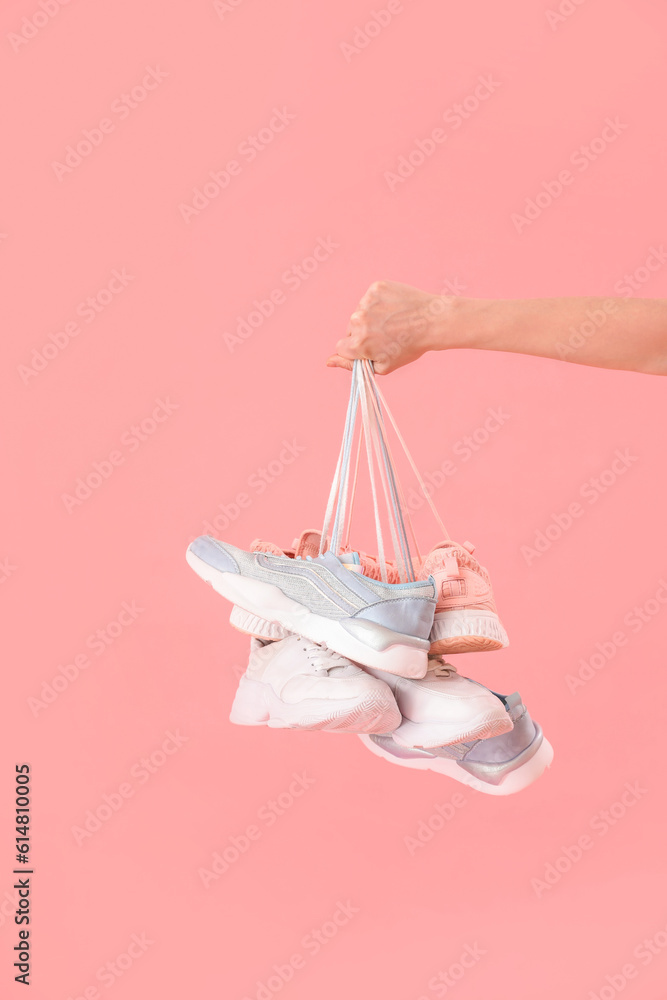 Female hand with many sneakers on pink background